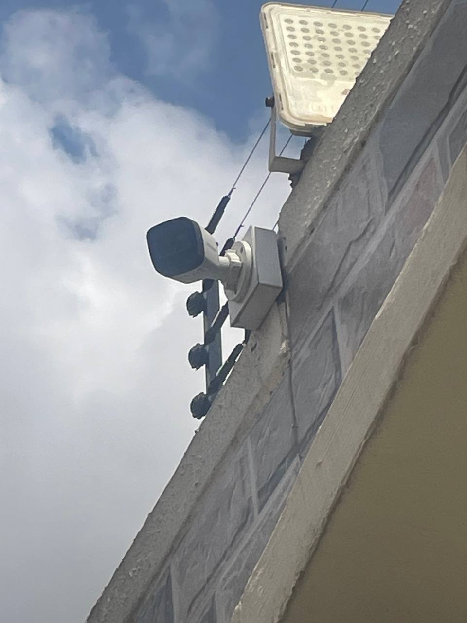 Surveillance camera and floodlight mounted on a perimeter wall